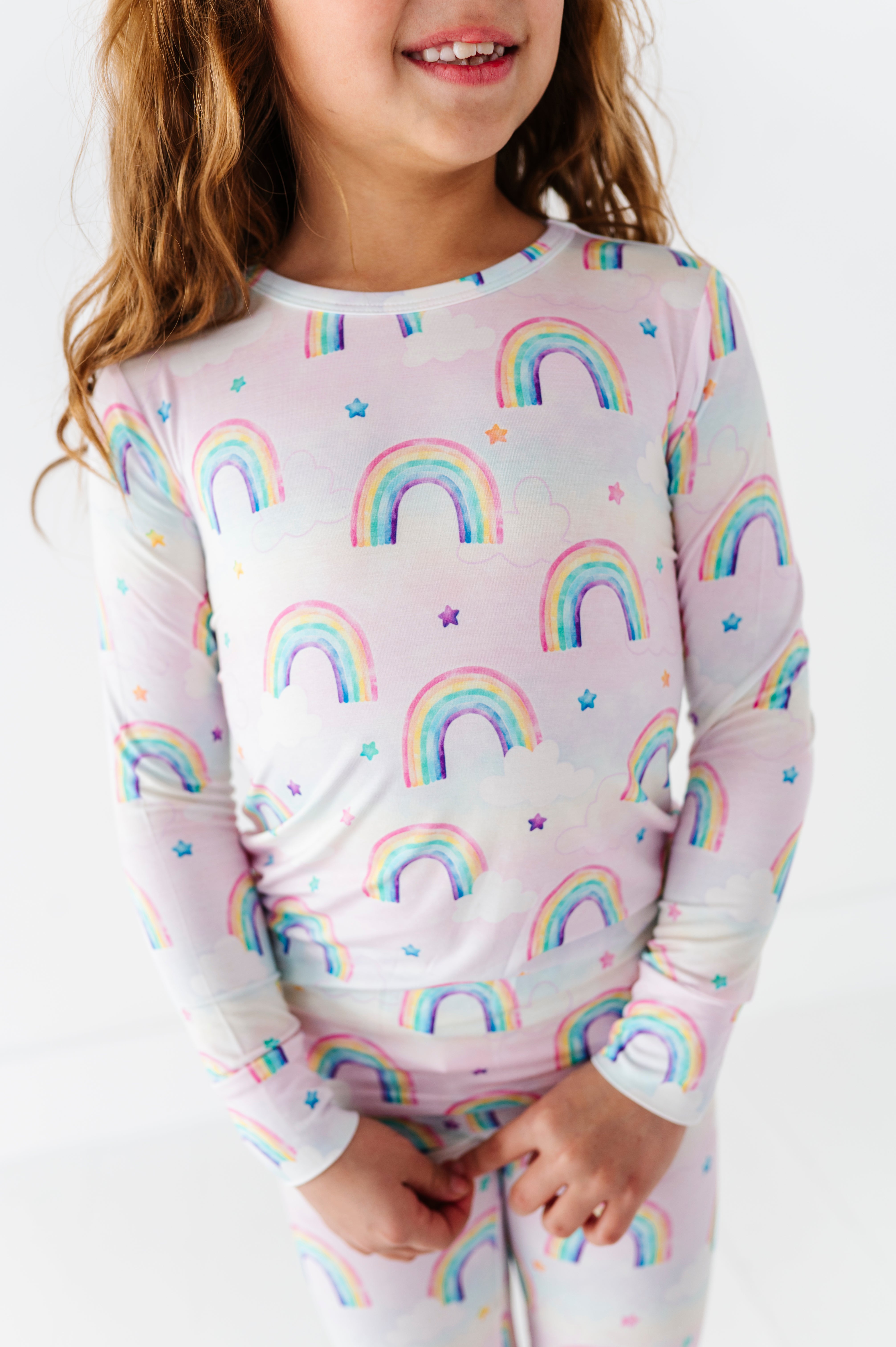 Child wearing a long-sleeve bamboo shirt and pants with watercolor rainbow pattern on a white background